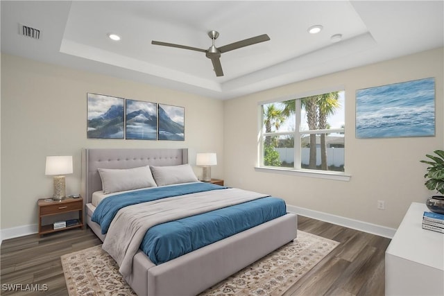 bedroom with a raised ceiling, baseboards, and dark wood-style flooring