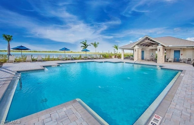 pool featuring a water view, a patio area, and fence