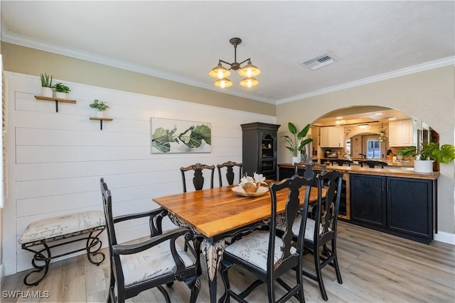 dining area with light wood-style floors, visible vents, arched walkways, and ornamental molding