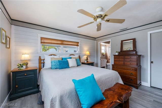 bedroom with ceiling fan, wood walls, wood finished floors, baseboards, and ensuite bath