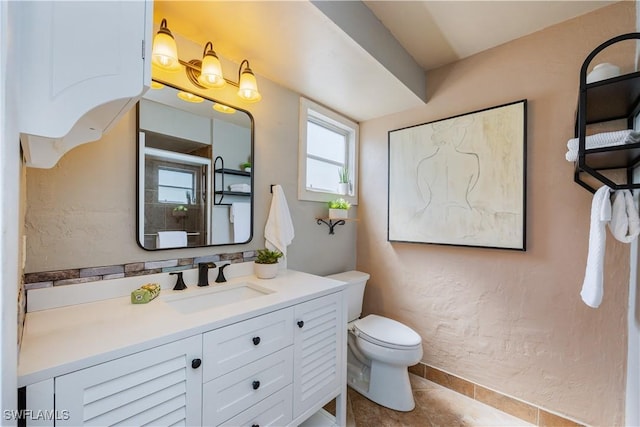 bathroom with a textured wall, tile patterned flooring, vanity, and toilet