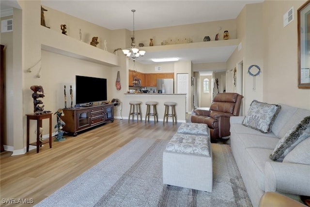 living room with a high ceiling, visible vents, baseboards, light wood finished floors, and an inviting chandelier