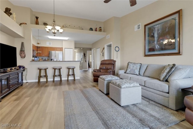 living room with ceiling fan with notable chandelier, light wood finished floors, visible vents, and baseboards