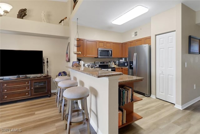 kitchen with a peninsula, a breakfast bar, visible vents, appliances with stainless steel finishes, and brown cabinets