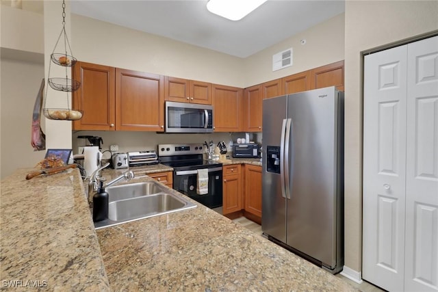 kitchen with stainless steel appliances, a sink, visible vents, light stone countertops, and brown cabinetry