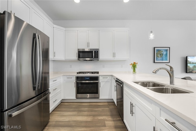 kitchen with stainless steel appliances, a sink, white cabinets, light countertops, and dark wood finished floors