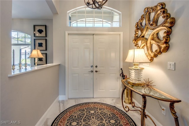 entryway with marble finish floor, baseboards, and a notable chandelier