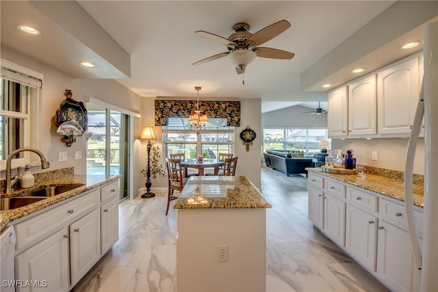 kitchen featuring recessed lighting, white cabinetry, a kitchen island, a sink, and light stone countertops