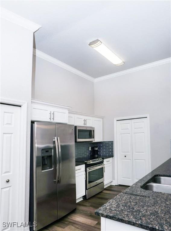 kitchen featuring stainless steel appliances, white cabinetry, ornamental molding, backsplash, and dark stone counters