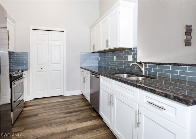 kitchen with stainless steel appliances, dark wood-type flooring, white cabinetry, a sink, and dark stone countertops