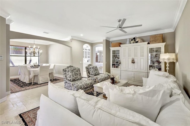 living room with baseboards, stone tile flooring, ornamental molding, and ceiling fan with notable chandelier