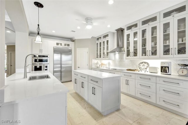 kitchen featuring a center island, ceiling fan, wall chimney range hood, appliances with stainless steel finishes, and a sink