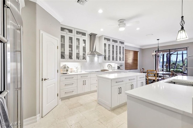 kitchen with a kitchen island, a sink, ornamental molding, wall chimney range hood, and ceiling fan with notable chandelier