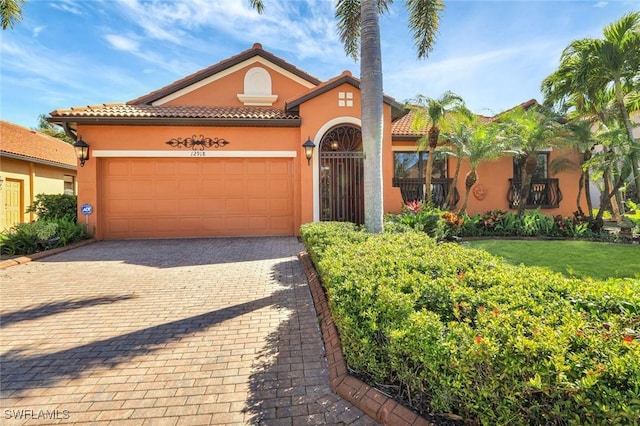 mediterranean / spanish-style house with a tile roof, decorative driveway, an attached garage, and stucco siding