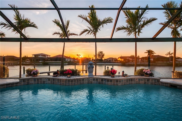 pool at dusk featuring glass enclosure, a water view, and an outdoor pool