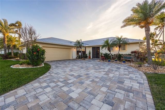 single story home with metal roof, decorative driveway, an attached garage, and stucco siding