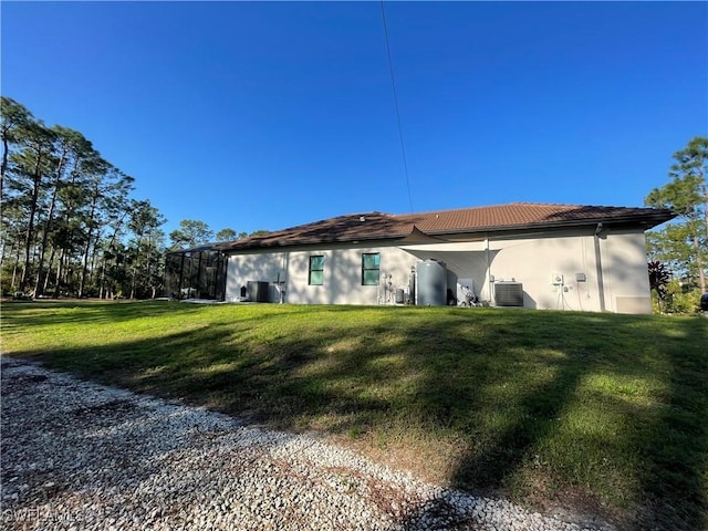 back of property with central AC unit, glass enclosure, a tile roof, a yard, and stucco siding