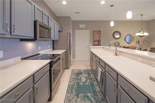 kitchen with light tile patterned floors, gray cabinetry, a sink, appliances with stainless steel finishes, and decorative light fixtures