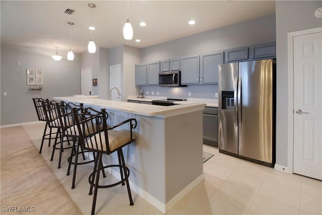 kitchen featuring a breakfast bar area, a kitchen island with sink, stainless steel appliances, light countertops, and a sink