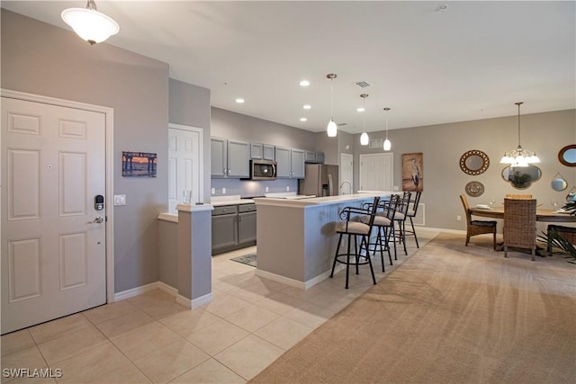 kitchen with a kitchen island with sink, light countertops, appliances with stainless steel finishes, gray cabinets, and a kitchen bar