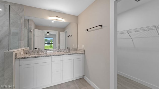 bathroom featuring a walk in shower, a sink, baseboards, a spacious closet, and double vanity