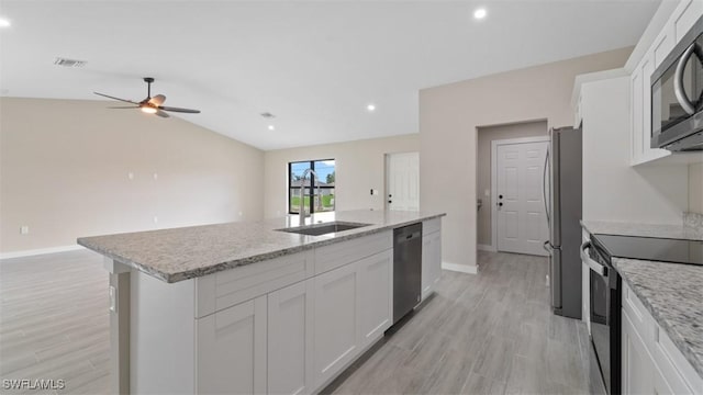 kitchen featuring appliances with stainless steel finishes, open floor plan, white cabinets, a sink, and an island with sink