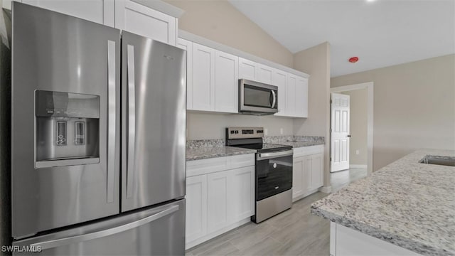 kitchen featuring vaulted ceiling, appliances with stainless steel finishes, light stone counters, and white cabinets