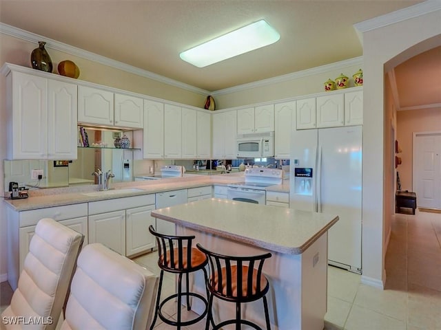 kitchen with light tile patterned flooring, white appliances, a kitchen island, a sink, and white cabinets