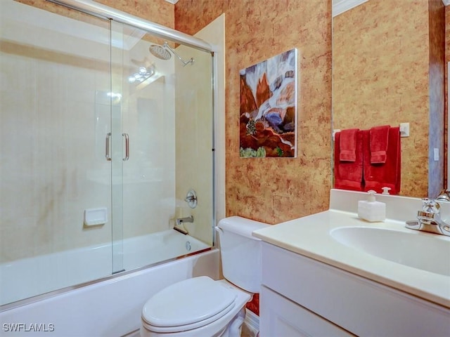 bathroom with toilet, enclosed tub / shower combo, vanity, and wallpapered walls