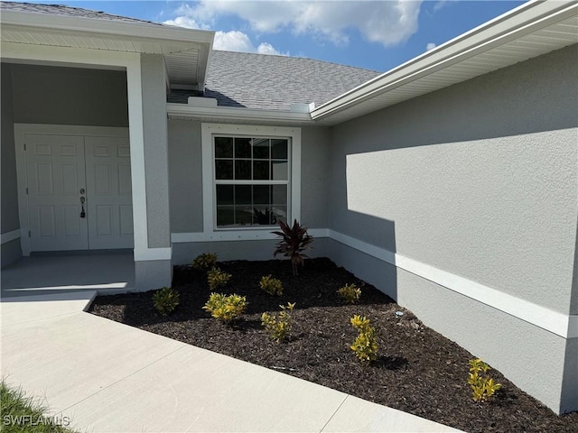 doorway to property featuring a shingled roof and stucco siding