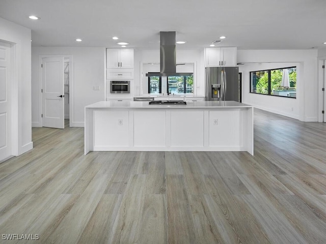 kitchen featuring island exhaust hood, plenty of natural light, stainless steel fridge, and white cabinetry