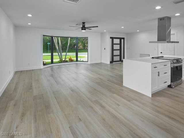 kitchen with white cabinets, stainless steel electric range oven, open floor plan, island exhaust hood, and light wood-style floors