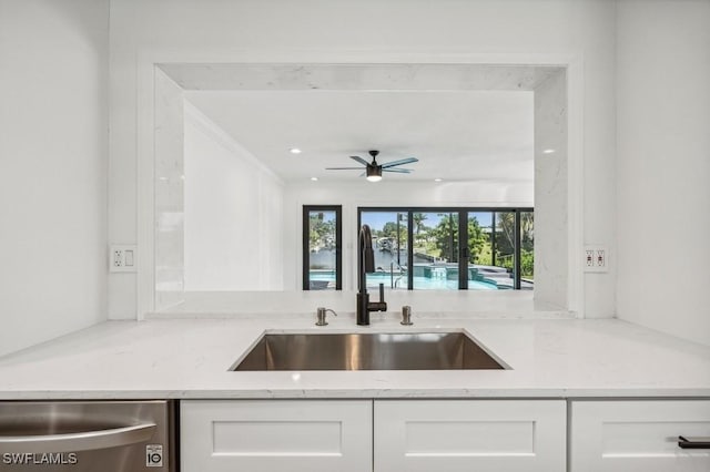 kitchen featuring stainless steel dishwasher, white cabinets, ceiling fan, a sink, and light stone countertops