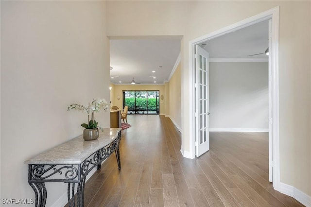 hallway featuring french doors, crown molding, baseboards, and wood finished floors