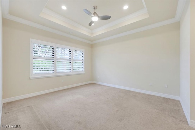 spare room featuring a tray ceiling, light colored carpet, ornamental molding, a ceiling fan, and baseboards