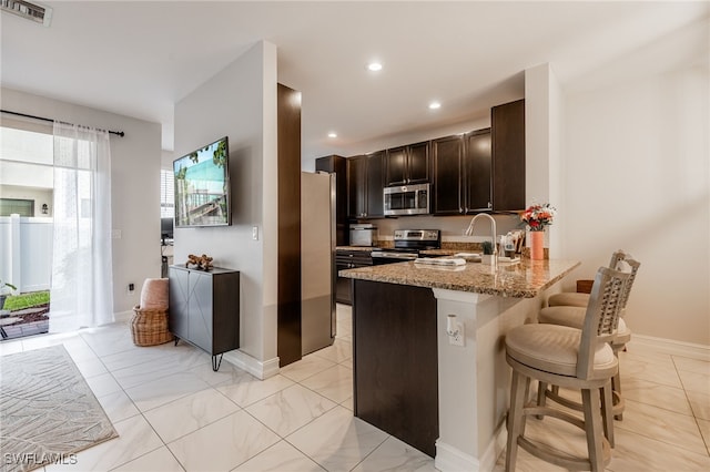 kitchen with dark brown cabinetry, stainless steel appliances, a breakfast bar, visible vents, and light stone countertops