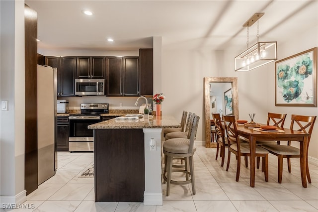 kitchen featuring appliances with stainless steel finishes, light stone counters, a peninsula, a kitchen bar, and a sink