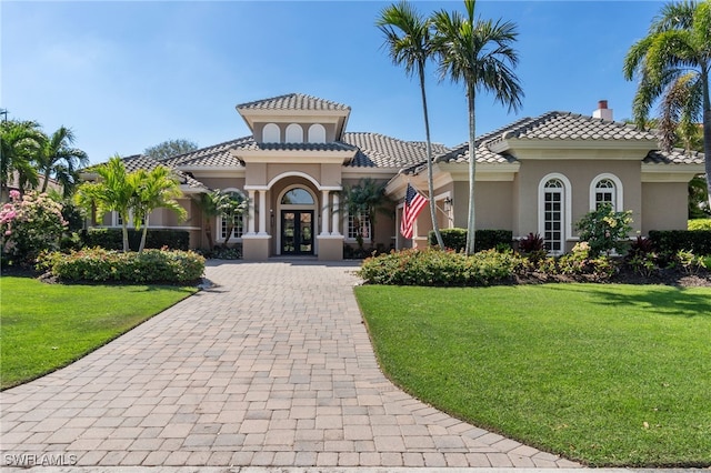 view of front of home with french doors, decorative driveway, stucco siding, a front lawn, and a chimney