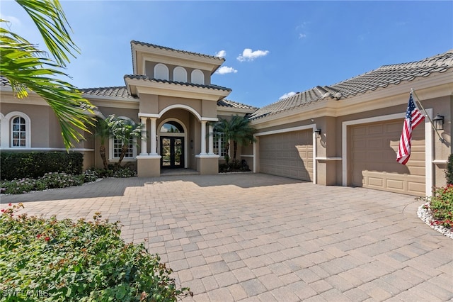 mediterranean / spanish-style home with a tile roof, stucco siding, french doors, decorative driveway, and an attached garage