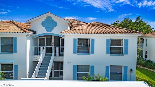 exterior space featuring a tile roof, stairs, and stucco siding