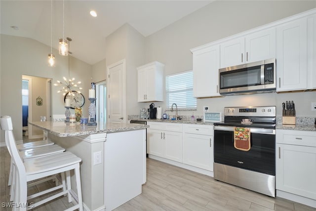 kitchen with appliances with stainless steel finishes, a kitchen island, light stone counters, and white cabinets