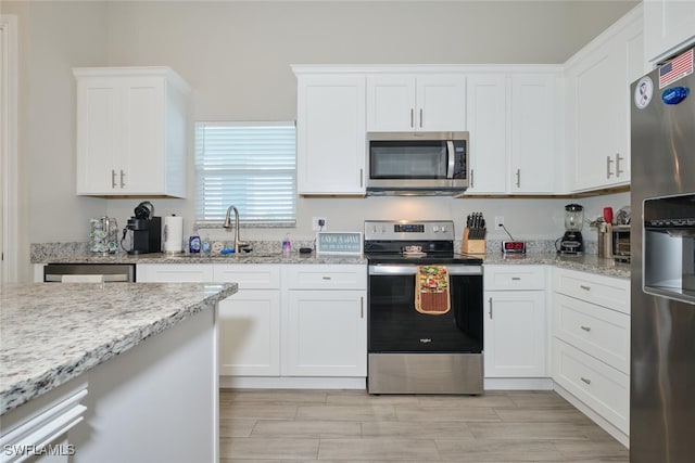 kitchen with appliances with stainless steel finishes, a sink, light stone counters, and white cabinets