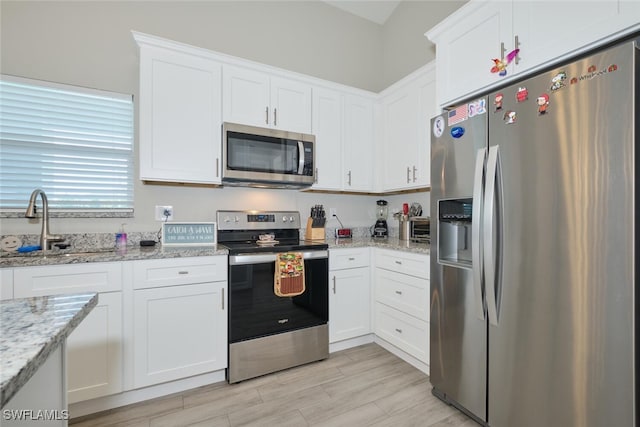 kitchen featuring appliances with stainless steel finishes, light wood-style floors, white cabinets, a sink, and light stone countertops