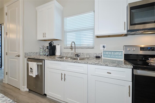 kitchen featuring light stone counters, white cabinetry, stainless steel appliances, and a sink