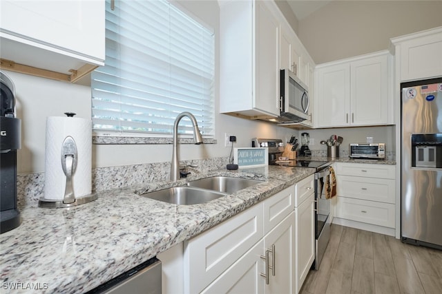 kitchen featuring a toaster, white cabinets, appliances with stainless steel finishes, light stone countertops, and a sink