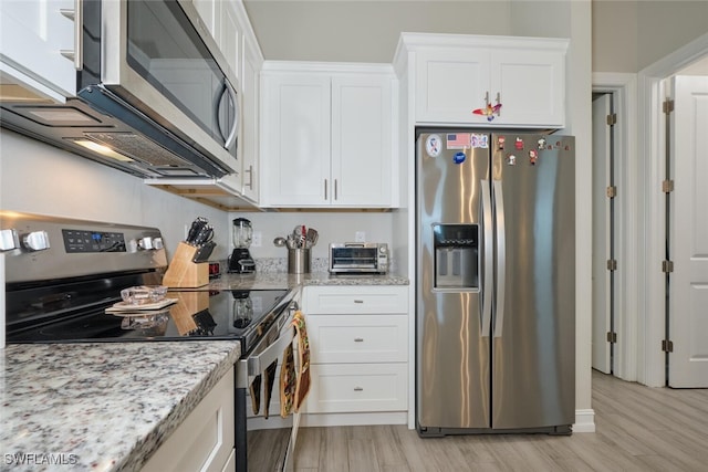 kitchen with a toaster, stainless steel appliances, white cabinets, light wood-type flooring, and light stone countertops