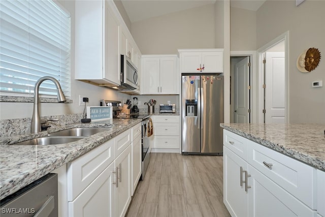 kitchen featuring lofted ceiling, light stone counters, a sink, white cabinetry, and appliances with stainless steel finishes