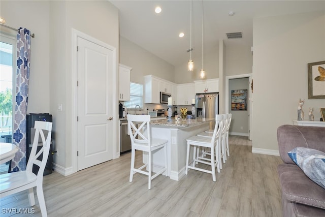 kitchen featuring visible vents, white cabinets, a breakfast bar, open floor plan, and stainless steel appliances