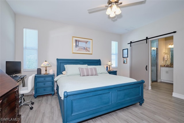 bedroom featuring connected bathroom, ceiling fan, light wood finished floors, and a barn door