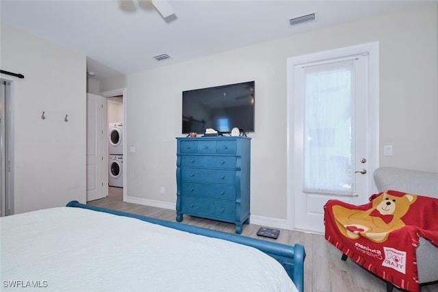 bedroom featuring stacked washing maching and dryer, wood finished floors, visible vents, and baseboards